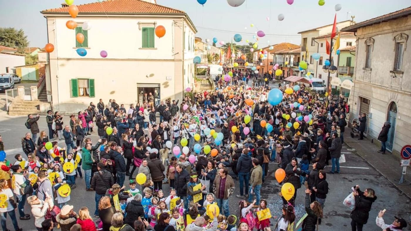 Hunderte Luftballons steigen über einer dicht gefüllten Dorfpiazza voller Familien bei einem Carnevale der letzten Jahre auf